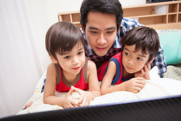 Father and son watching TV on bed