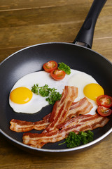 Scrambled eggs and bacon on frying pan on table close-up