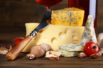 Pink wine and different kinds of cheese on wooden background
