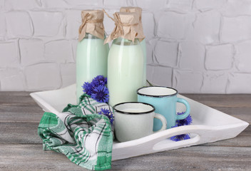 Bottles and cups of milk with cornflowers on wooden tray