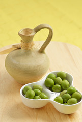 Olives in white playe with a jar on the wooden plate