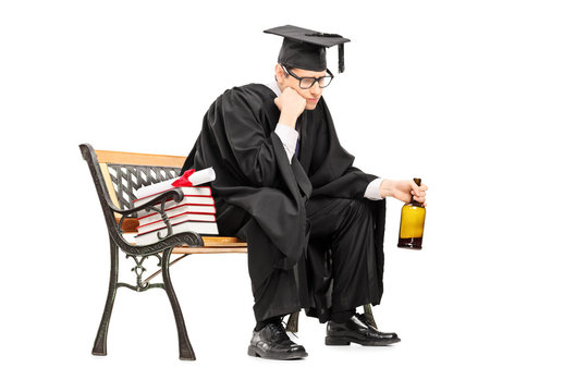 Sad college graduate drinking alcohol seated on bench