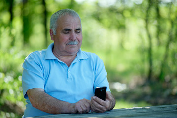 Naklejka na ściany i meble Elderly man smiling as he reads an sms