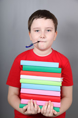 Boy with a pen in his mouth holding a stack of books
