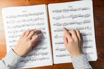 Naklejka premium Female hands sight reading sheet music on wooden background