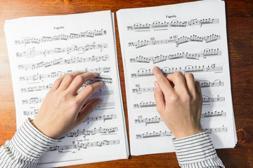 Female hands sight reading sheet music on wooden background