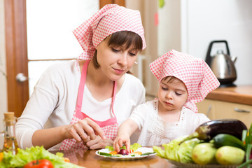 mother and kid girl making funny face from vegetables on plate
