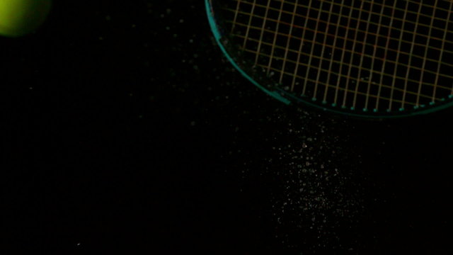 Tennis racket hitting a ball on black background