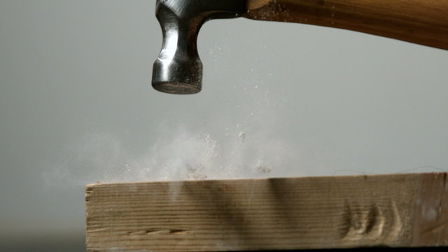 Hammer hitting a nail into wooden plank