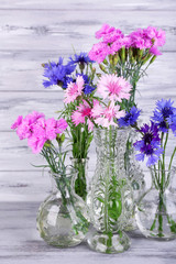 Beautiful summer flowers in vases on grey wooden background