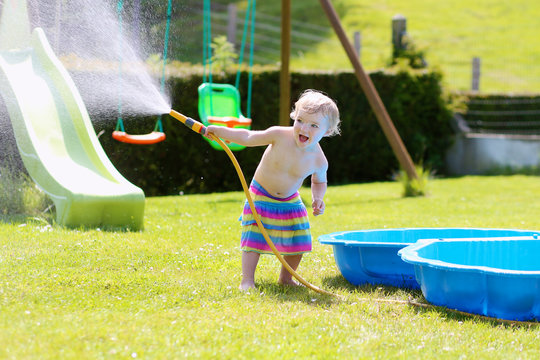 Happy little girl playing with water hose in the garden
