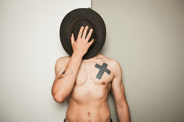 Young shirtless man hiding behind cowboy hat