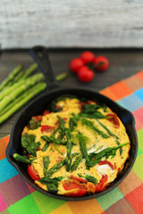 Omelette with asparagus and tomato on frying pan