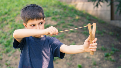 Child aiming with sling outdoors portrait. - 65500979