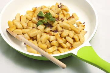 Potato dumplings on the green frying pan with wooden spoon