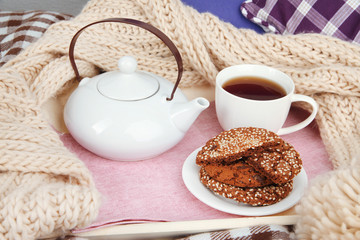 Obraz na płótnie Canvas Cup and teapot with cookies on tray and scarf on bed close up