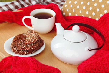 Cup and teapot with cookies on tray and scarf on bed close up