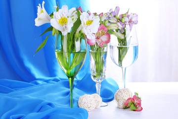 Freesias in glasses on table on fabric background