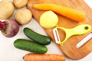 Peeler and raw vegetables on wooden table