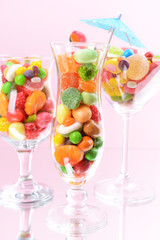 Different colorful fruit candy in glasses on pink background