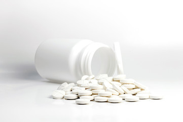 White pills out of pill bottle on white background