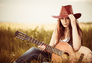 young stylish cowgirl with guitar at spring meadow