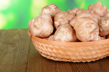 Topinambur roots in wicker basket on table on bright background