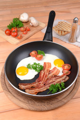 Scrambled eggs and bacon on frying pan on table close-up