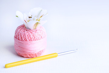 Colorful clew, crochet hook and fresh flower on light