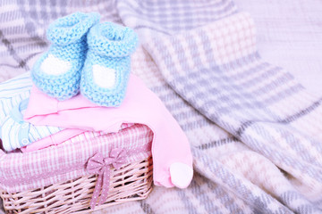 Baby clothes in basket on plaid in room