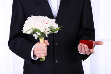 Man holding wedding bouquet and rings on light background