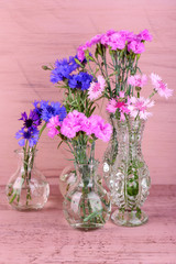Beautiful summer flowers in vases on pink wooden background