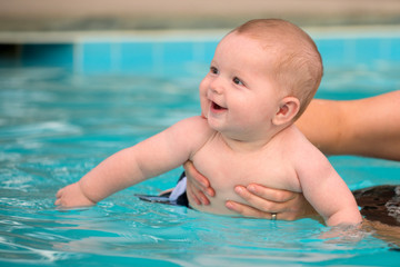 Fototapeta na wymiar Happy infant baby boy enjoying his first swim in pool