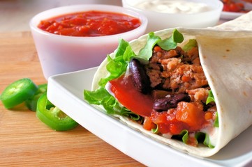 Close up of a burrito on a plate filled with meat and vegetables