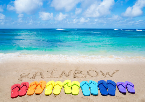 Sign "Rainbow" and color flip flops on sandy beach