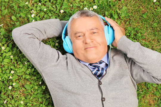 Mature Man With Headphones Lying On Grass