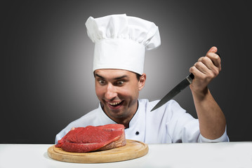 Crasy chef looking at piece of raw meat with a knife in his hand