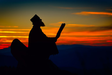 silhouette of priest reading in the sunset light