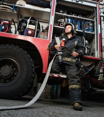 Firefighter near truck with equipment with water hose 