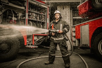Fototapeta premium Firefighter holding water hose near truck with equipment