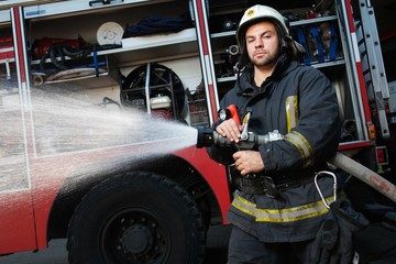 Firefighter holding water hose near truck with equipment