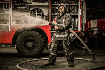 Firefighter holding water hose near truck with equipment