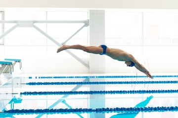 Young muscular swimmer jumping from starting block