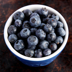 Blueberries in blue bowl on brown background