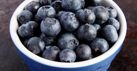 Blueberries in blue bowl on brown background