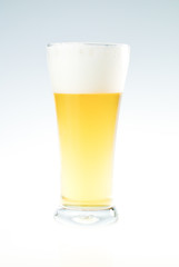 Glass of fresh beer with cap of foam on white background