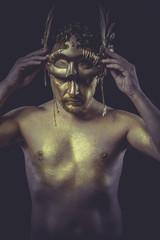 Fototapeta na wymiar Golden, Man with body painted gold feather mask and steel sword