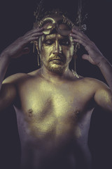 Fototapeta na wymiar Fashion, Man with body painted gold feather mask and steel sword