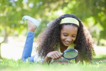 Young girl looking at grass through magnifying glass in the park