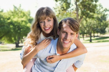 Man giving his pretty girlfriend a piggy back in the park smilin